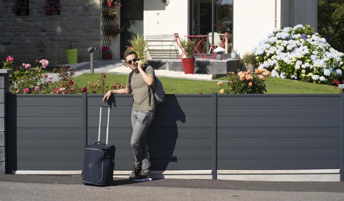 Etudian appuyé sur une clôture en composite Silvadec, au téléphone, une valise à la main.